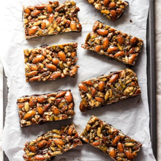 Nut and seed granola bars that have been dipped in chocolate laid in rows on white parchment paper.