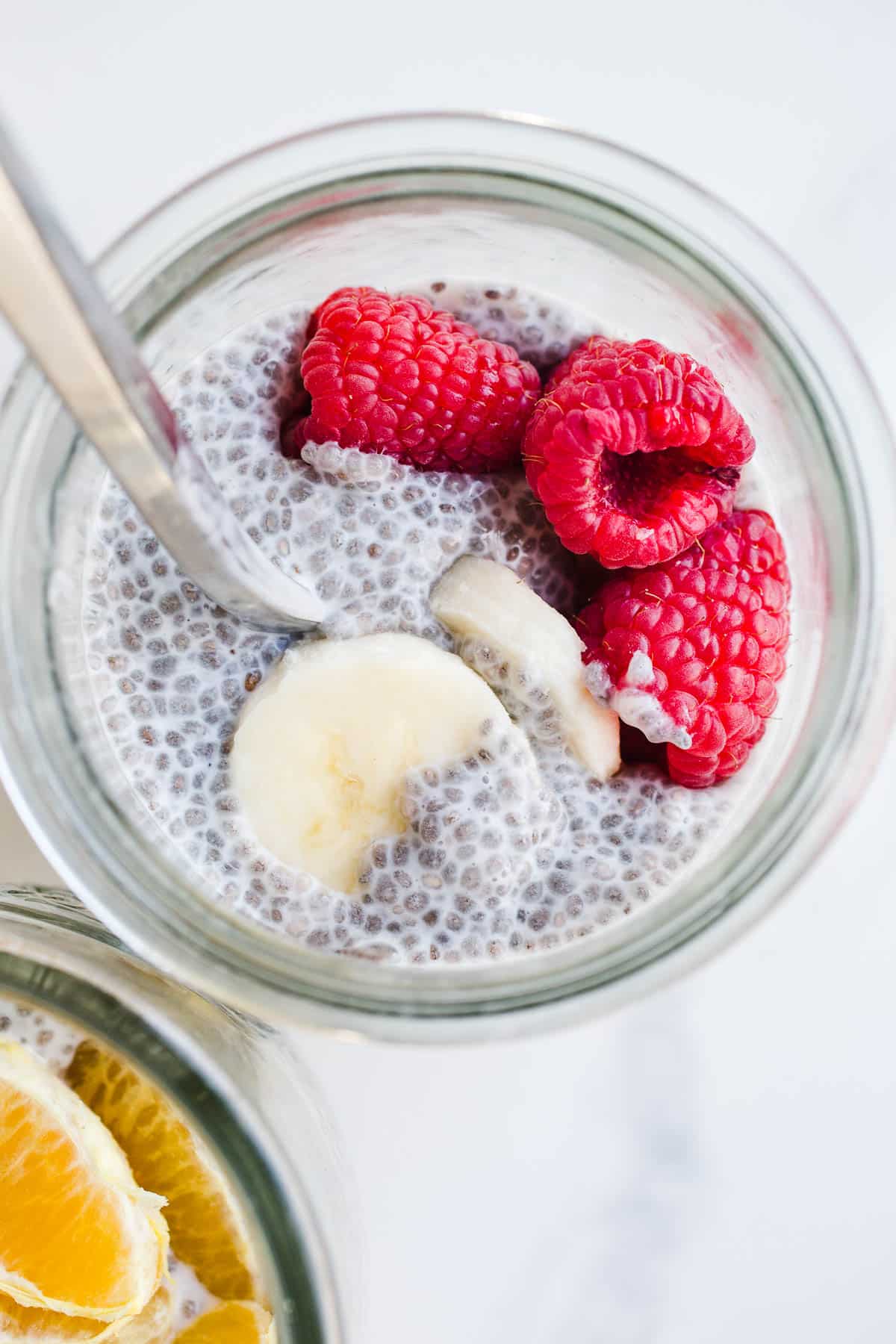 A jar filled with chia pudding and topped with fresh raspberries and bananas. 