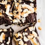 Chocolate brownies with toasted coconut on top on parchment paper.