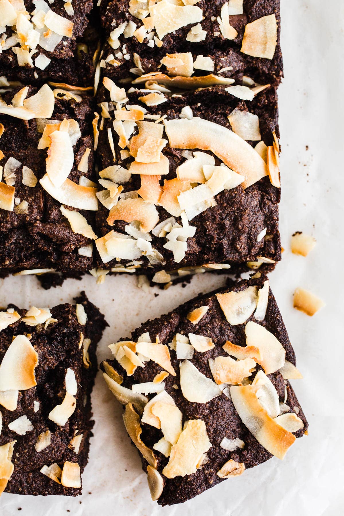 Chocolate brownies with toasted coconut on top on parchment paper.