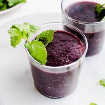 Frozen blueberry mojito in a rocks glass with a sprig of mint stuck into the drink as a garnish.