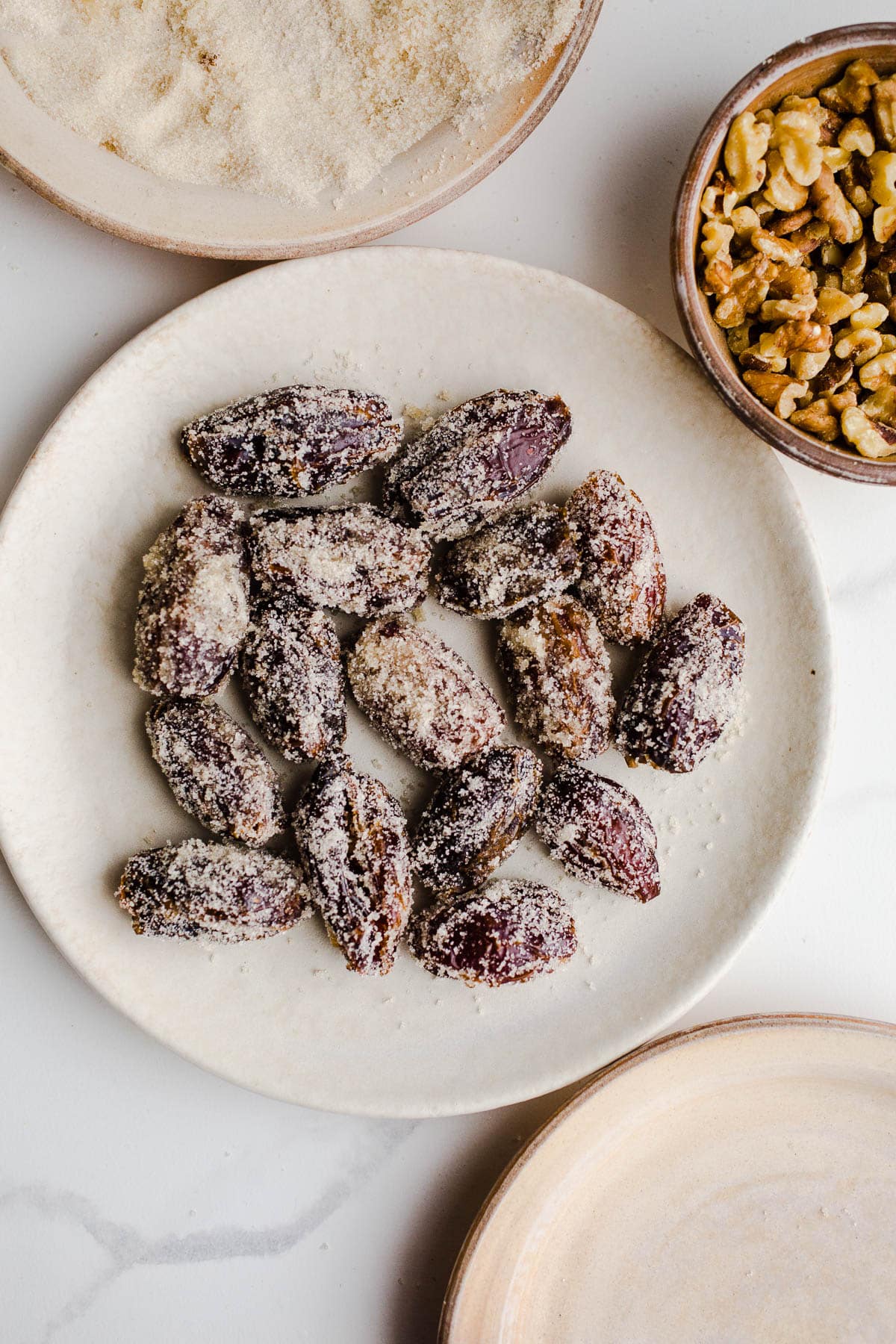 Sugared Dates on a plate next to a small bowl of walnuts.
