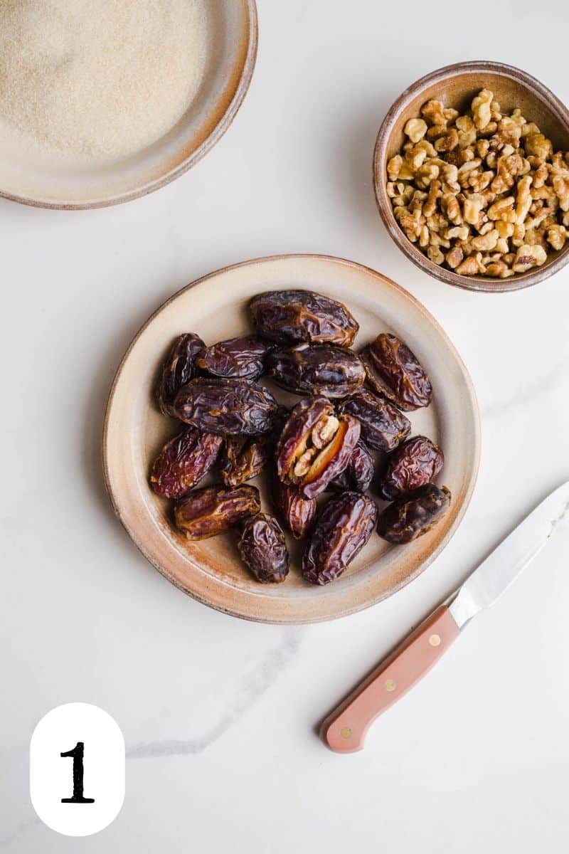 Dates on a plate and walnuts in a small bowl on a marble surface.