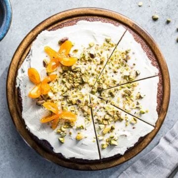 A cake topped with whipped cream, pistachios, and kumquats.