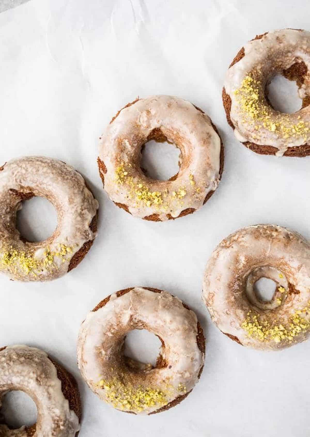 Coffee cake donuts with icing and pistachios on a piece of parchment paper.