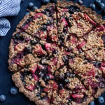 A crumble tart with strawberries and blueberries sitting on a blue tablecloth.