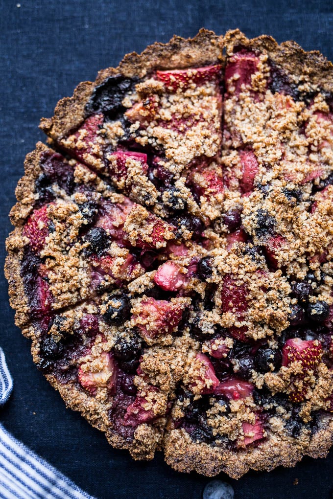 A gluten-free mixed berry tart with almond flour crumble on top place on a blue tablecloth.