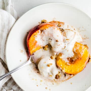 Peach halves in a bowl with ice cream and walnuts.