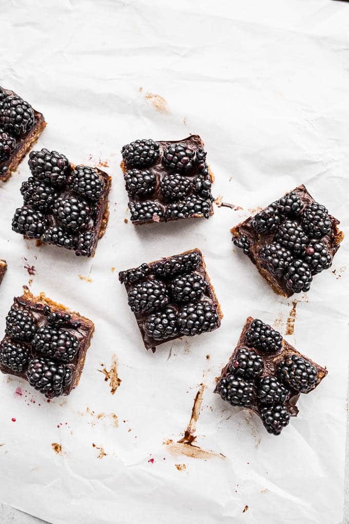 Oat bars topped with chocolate and blackberries on a piece of white parchment paper.
