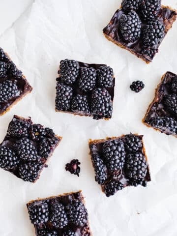 Date and nut bars topped with blackberries on parchment paper.