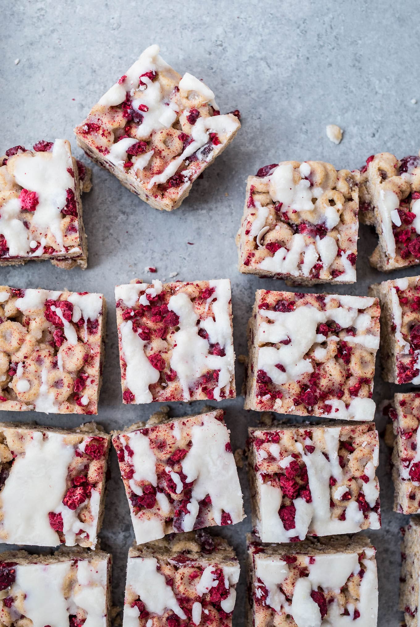 Cereal treats with raspberries and icing on a blue surface.