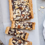 A tart filled with jam and topped with almonds on a piece of parchment paper.