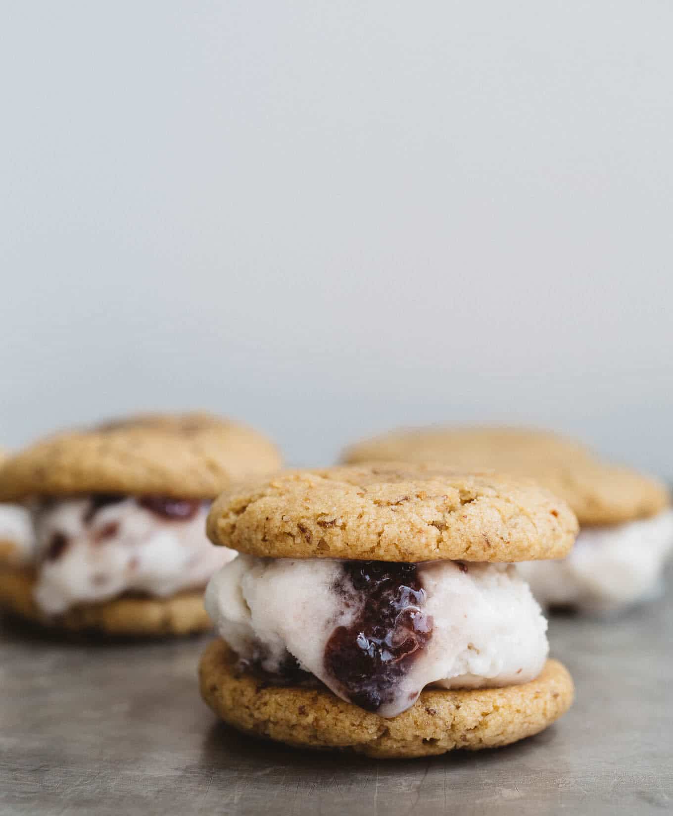 Peanut Butter and Jelly Ice Cream Sandwiches! Soft and chewy, maple-sweetened peanut butter cookies sandwiched around homemade vegan jam ice cream. Gluten-free, vegan, and refined sugar-free.