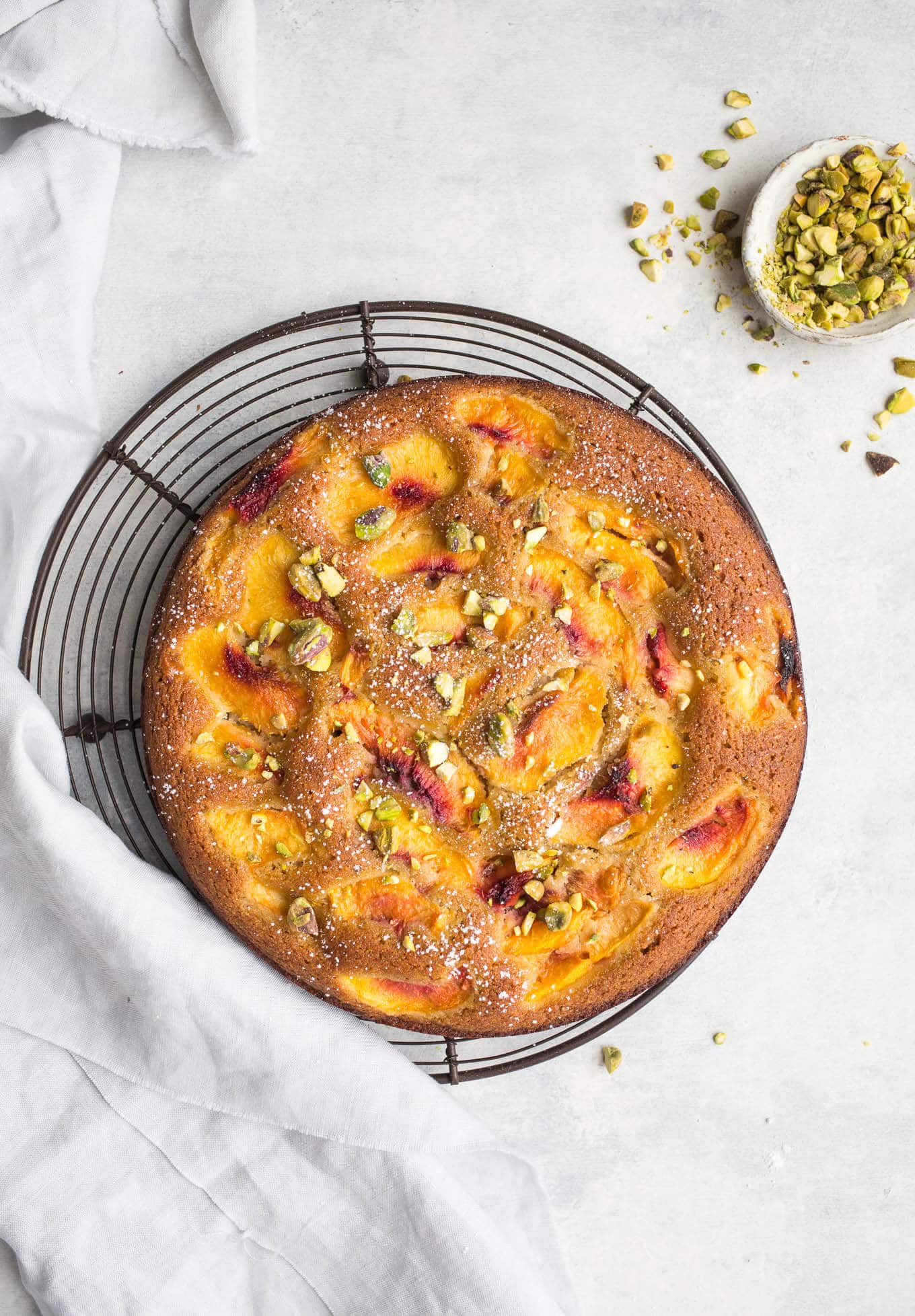 A gluten-free peach cake and pistachios on a wire rack.