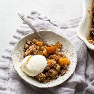 Baked crisp with apples and butternut squash in a white bowl with a scoop of ice cream.