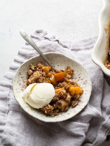Baked crisp with apples and butternut squash in a white bowl with a scoop of ice cream.
