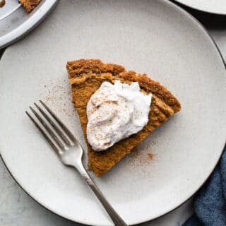 A slice of gingersnap pumpkin pie on a gray plate with a blue napkin and fork.