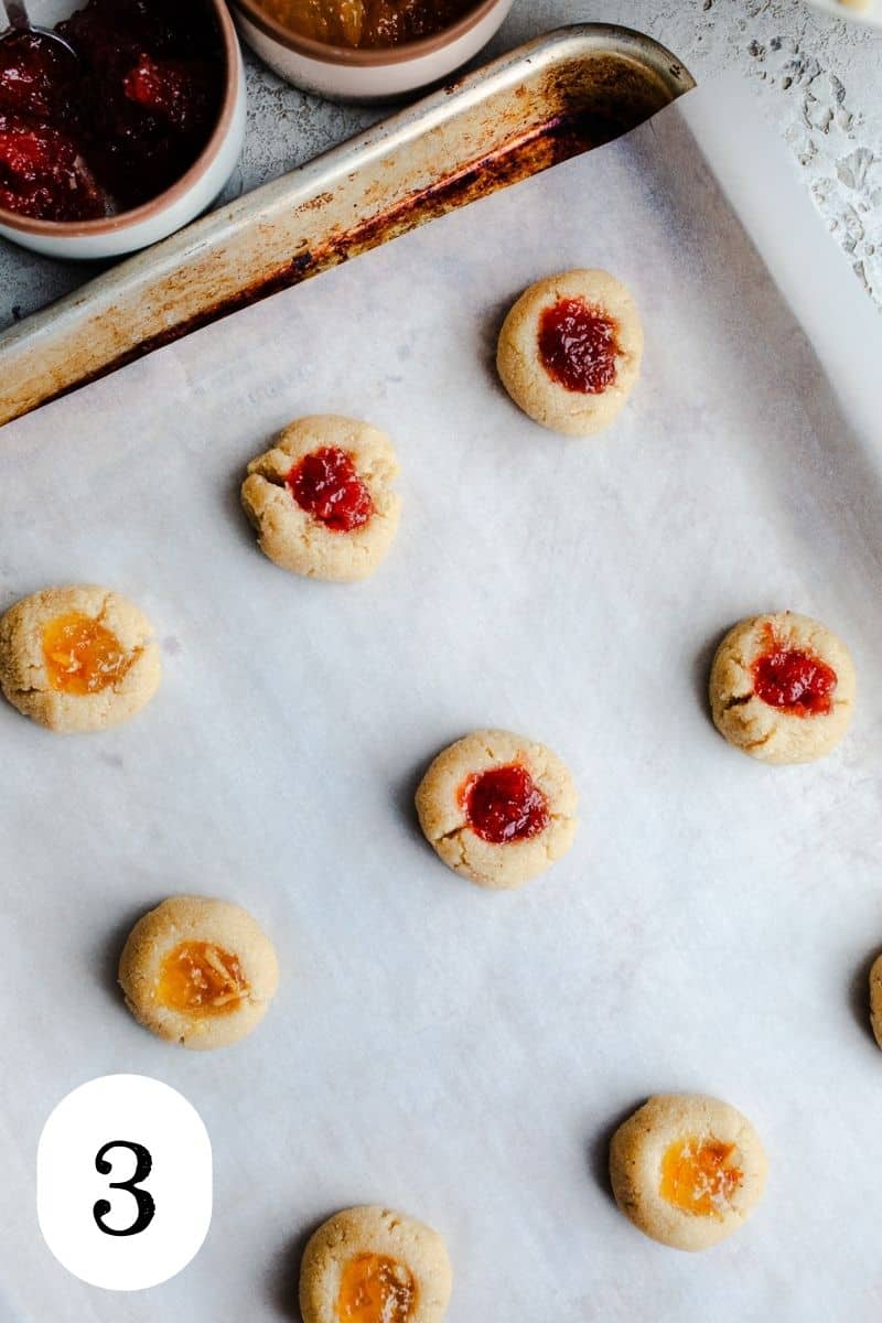 Filled thumbprint cookies on a baking sheet. 