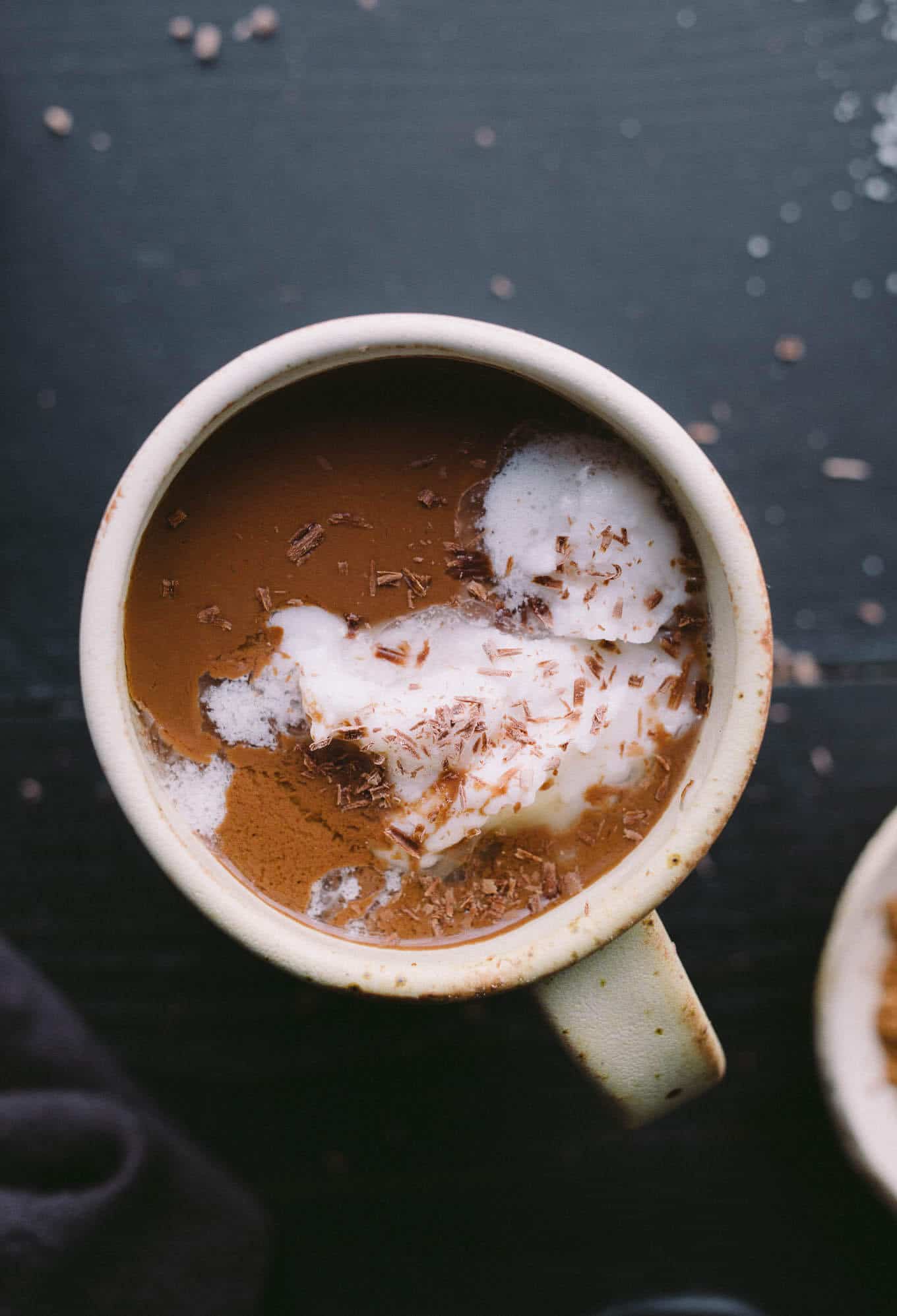 Hot cocoa in a mug topped with coconut cream and chocolate shavings.