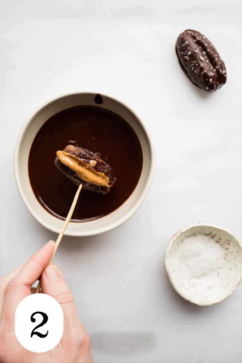 A stuffed date being dipped in chocolate.