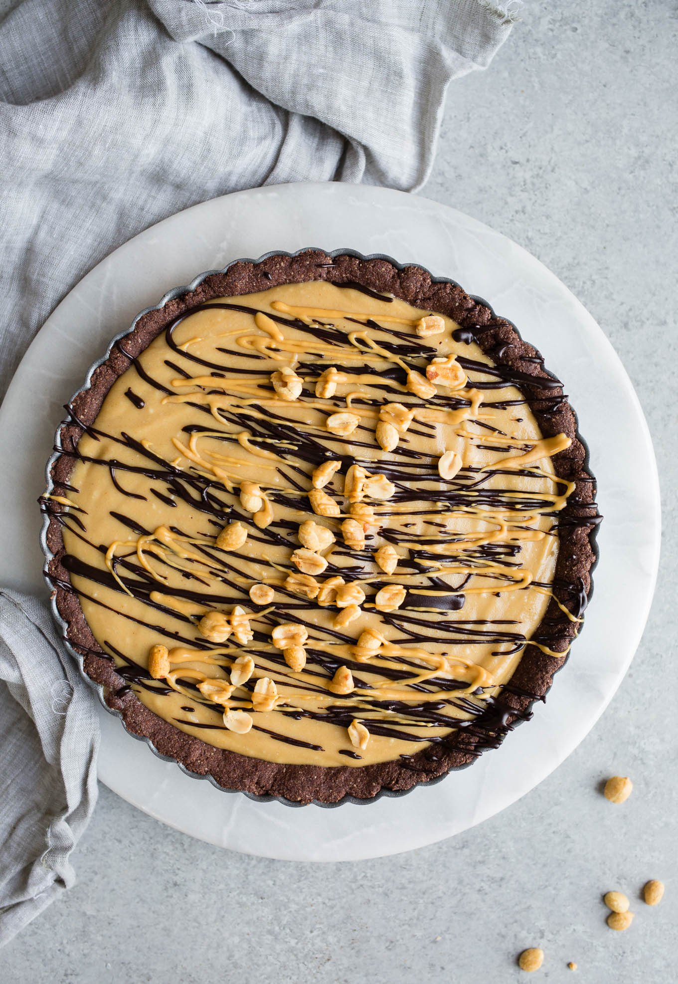 A frozen pie with a chocolate crust set on a marble round and a gray linen tea towel.