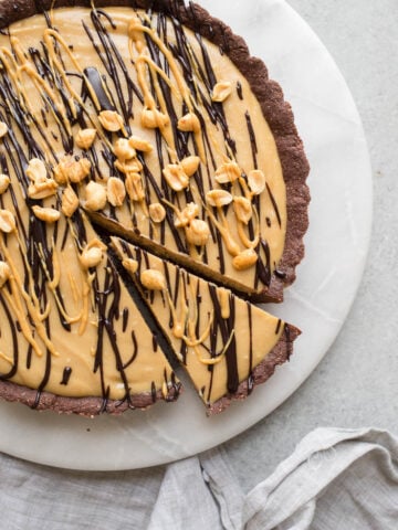 A peanut butter pie with chocolate crust drizzled with chocolate sauce and melted peanut butter on top of a marble round.