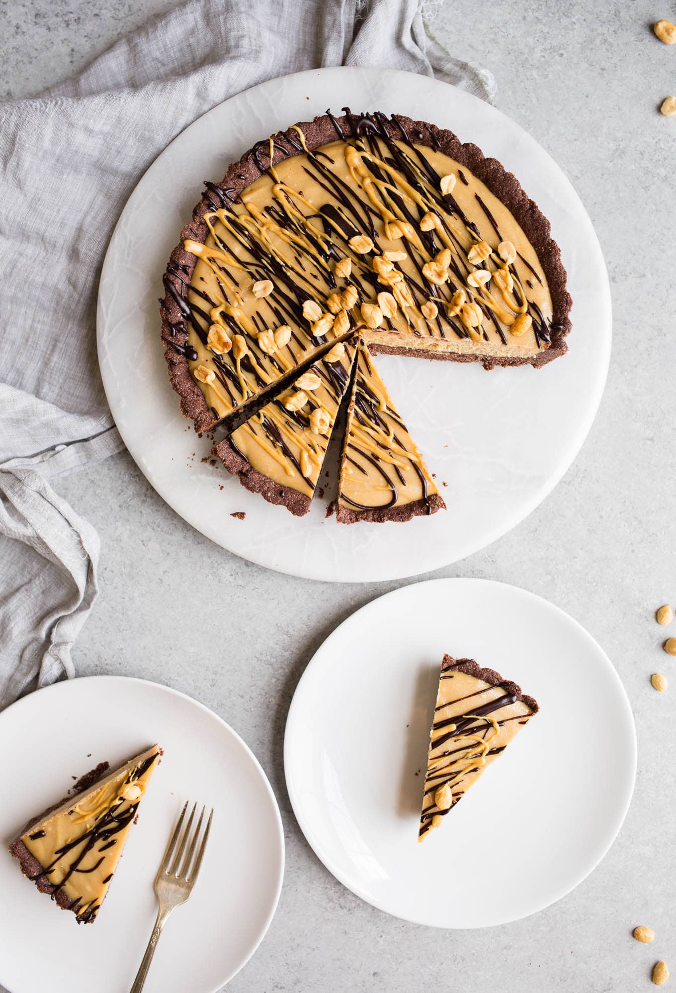 A frozen pie in an almond flour chocolate crust on a marble round with two slices of pie on white plates.
