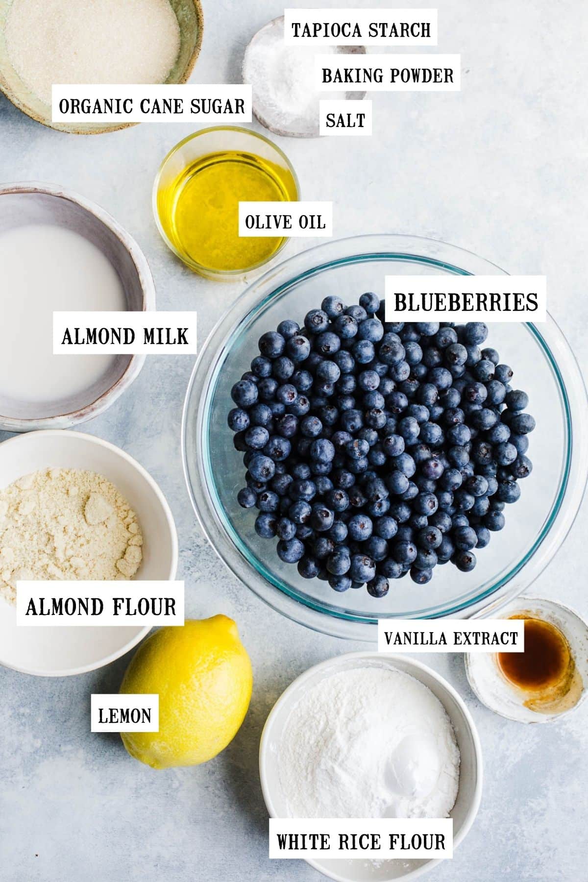 Blueberries, almond flour, milk, olive oil, sugar, vanilla, and tapioca starch in different sized bowls.
