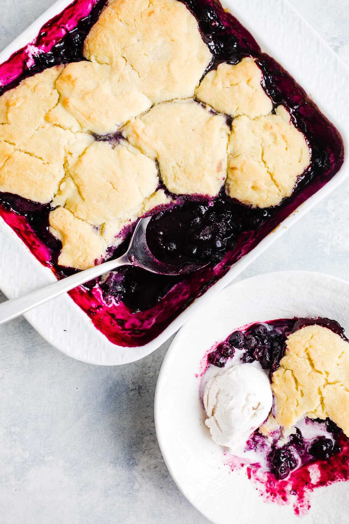 Golden brown biscuits on top of baked blueberry filling in a white baking dish.