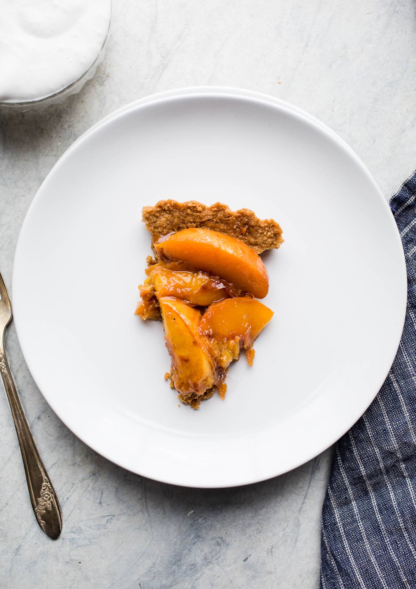 Roasted Peach Tart made with a gluten-free graham cracker crust, peaches roasted with coconut sugar, and served with a ginger-flavored coconut whipped cream. Simple and delicious! Gluten-free, vegan, refined sugar-free. 