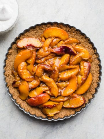 Roasted Peach Tart made with a gluten-free graham cracker crust, peaches roasted with coconut sugar, and served with a ginger-flavored coconut whipped cream. Simple and delicious! Gluten-free, vegan, refined sugar-free. 