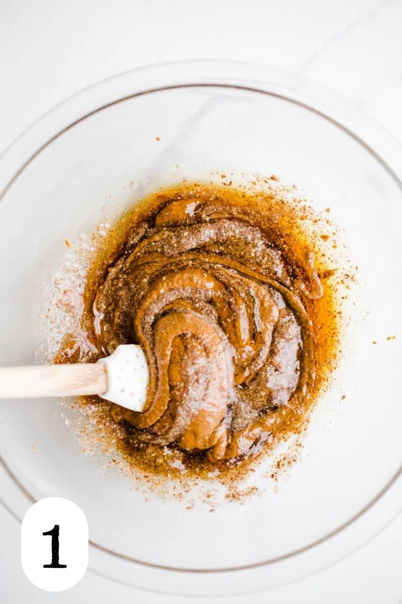 Almond butter and maple syrup being stirred together in a glass bowl. 