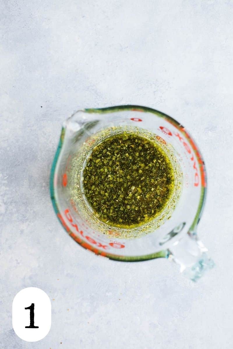 Olive oil and herbs in a glass measuring cup.