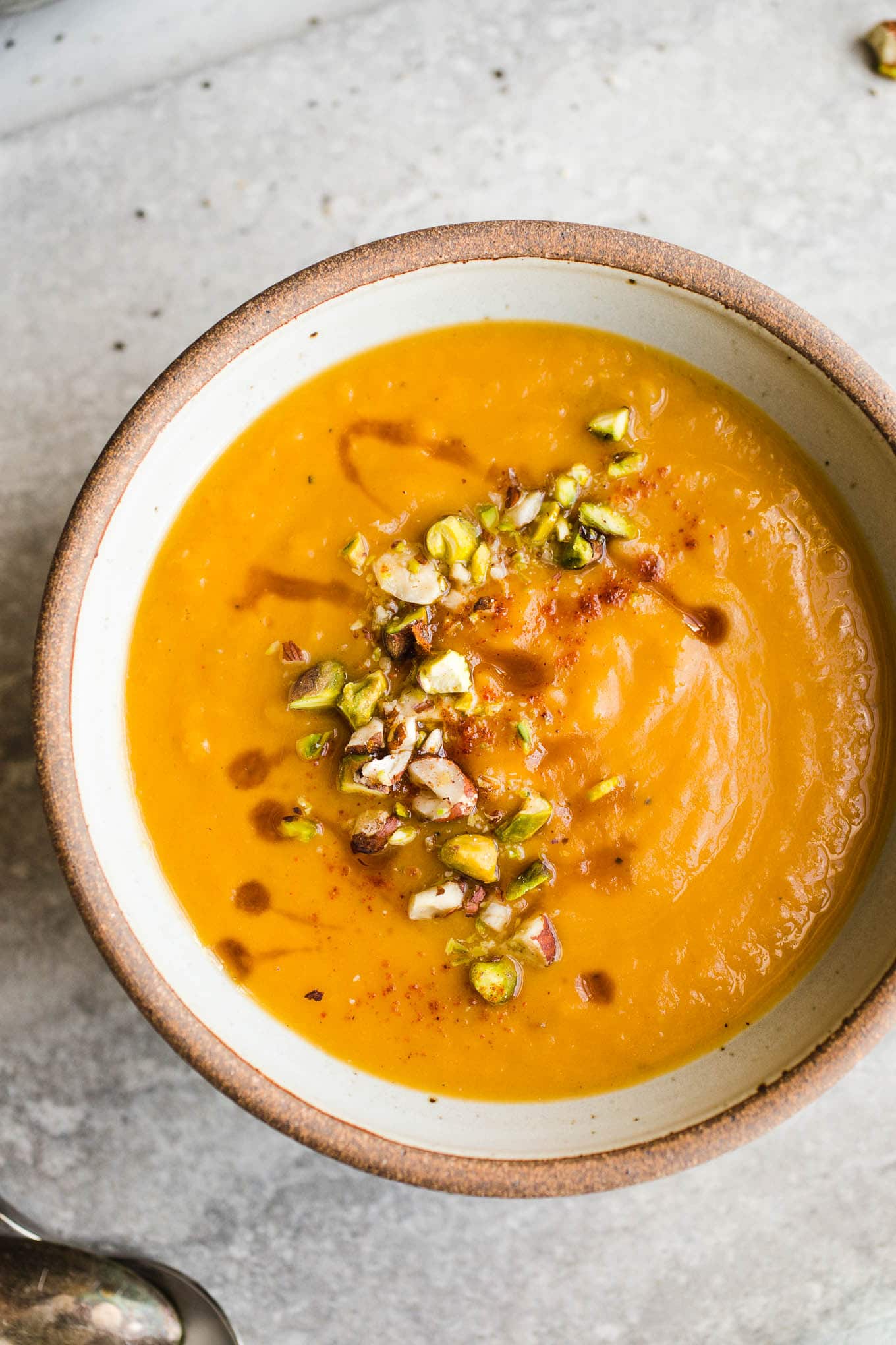 A rustic bowl filled with orange sweet potato soup and garnished with chopped nuts.