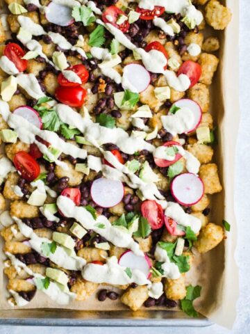 Tater tot nachos loaded with toppings on a pan.