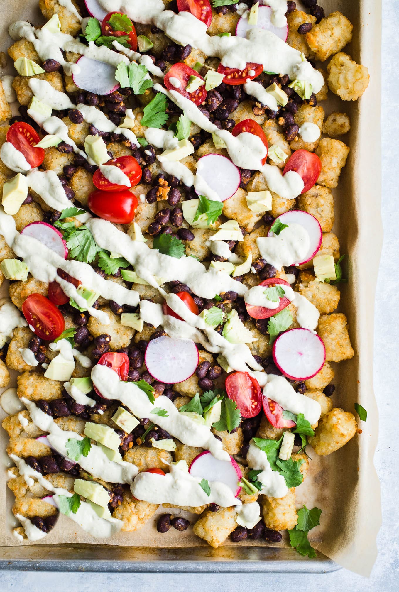 Tater tot nachos loaded with toppings on a baking sheet.