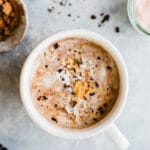 Toasted coconut hot chocolate in a mug topped with coconut cream, toasted coconut, and chocolate shavings.