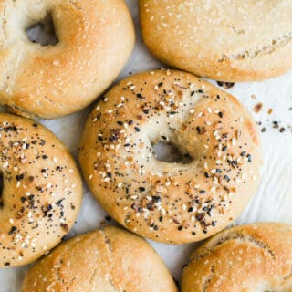 Bagels topped with seeds on a piece of parchment paper.