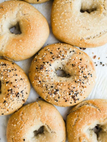 Bagels topped with seeds on a piece of parchment paper.