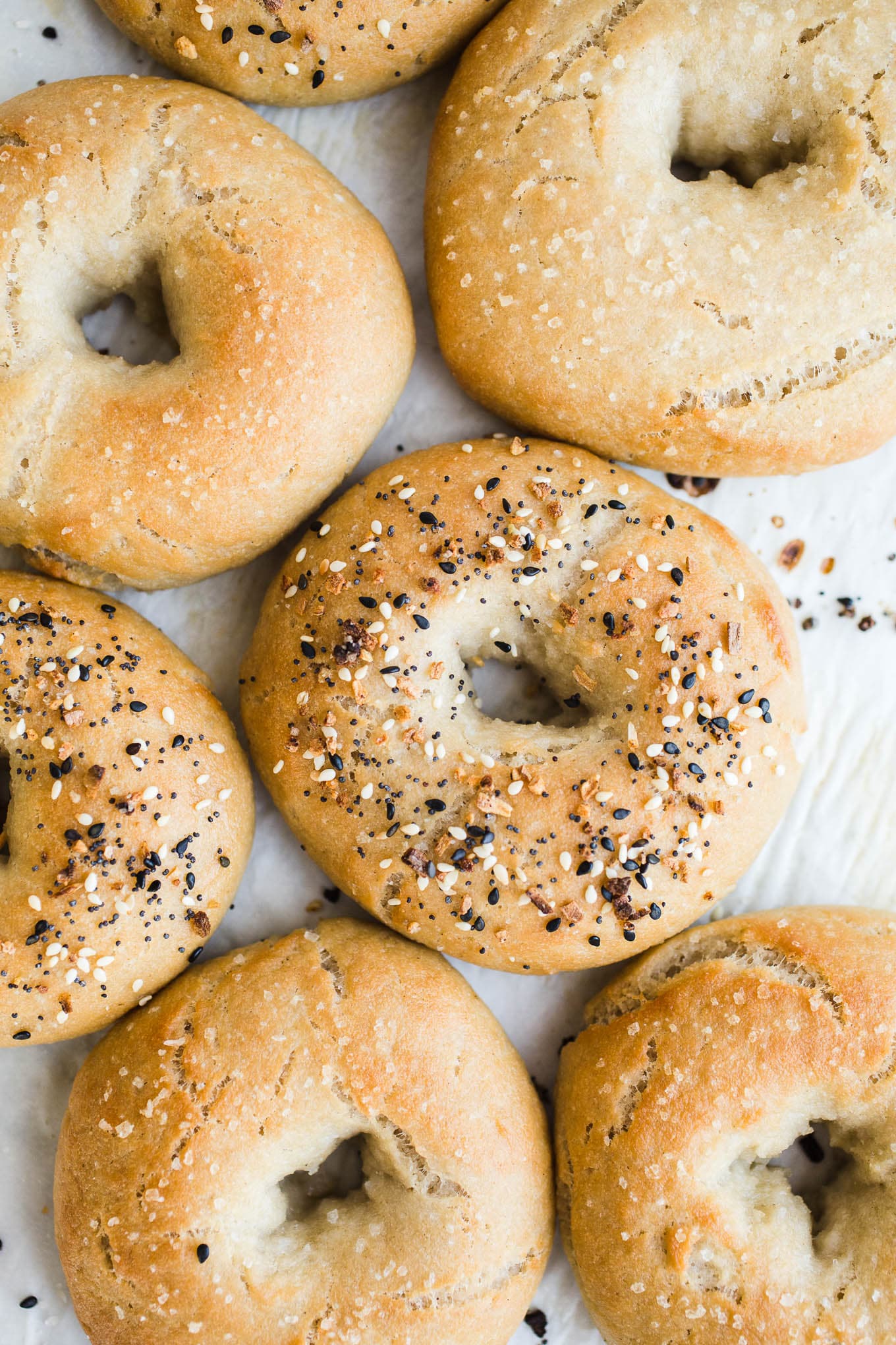 Bagels topped with seeds on a piece of parchment paper.