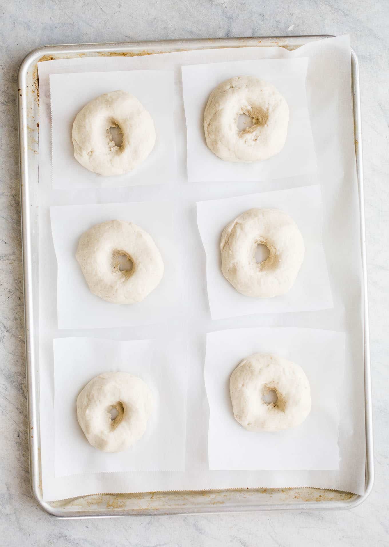 Proofed bagels on a baking sheet. 