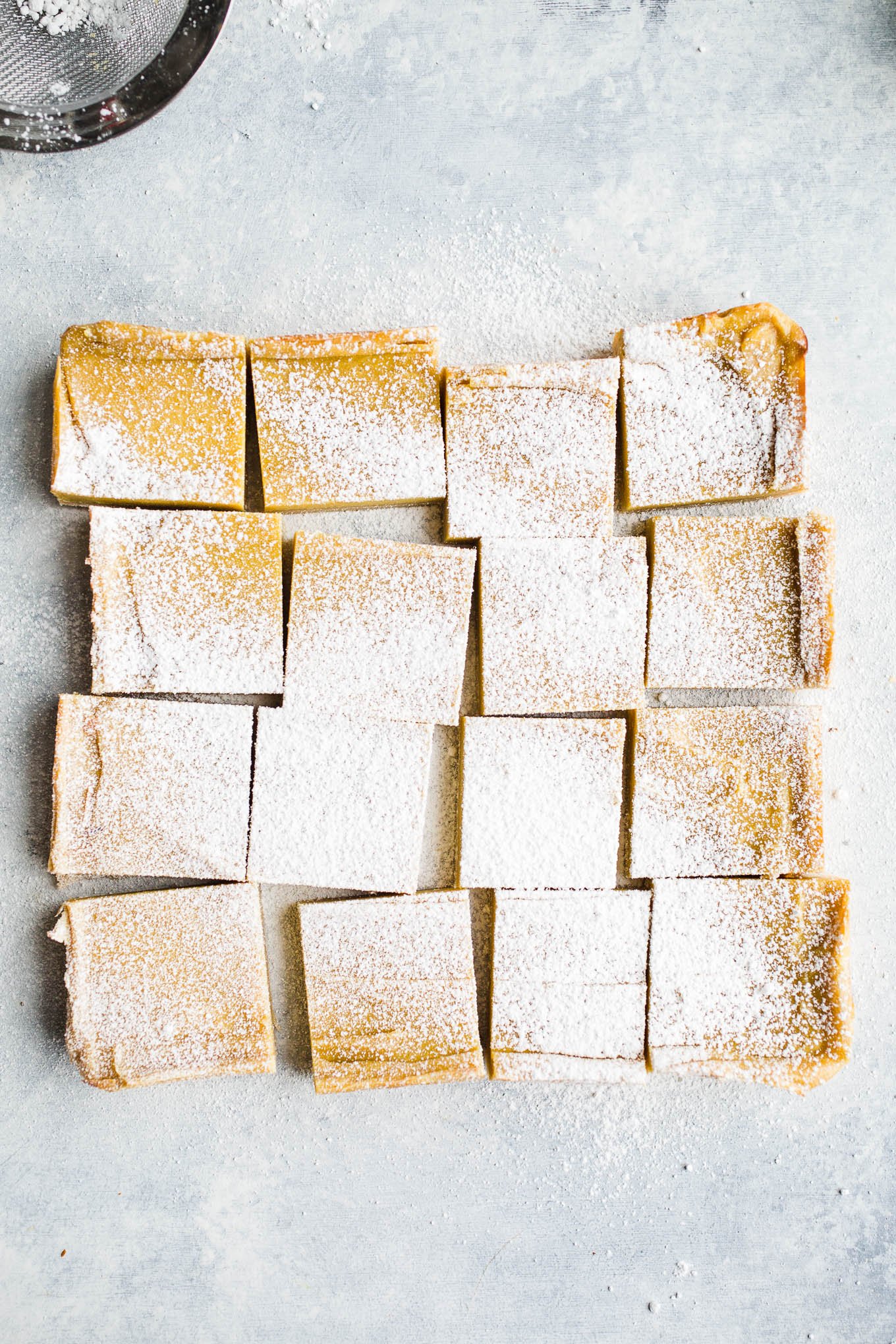 Lemon bars dusted with powdered sugar on a light blue surface. 