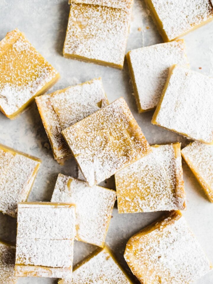 Lemon bars topped with powdered sugar spread out on a blue surface.
