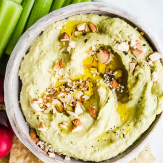 Green hummus in a bowl with veggies.