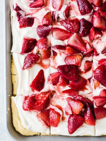 A three-layer sheet pan cake with coconut whipped cream and roasted strawberries on top.