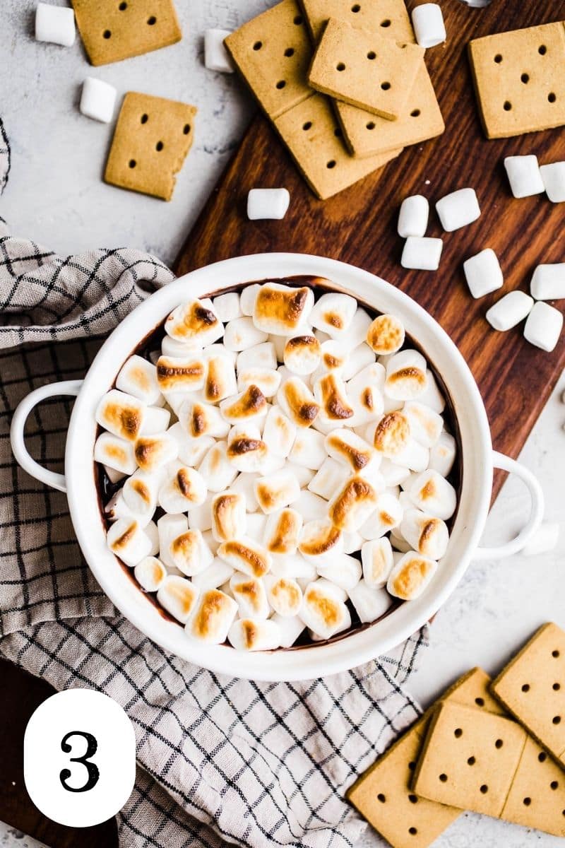 Golden brown mini marshmallows on top of chocolate dip in white casserole dish.