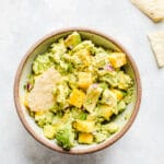 A bowl of guacamole with mango chunks.