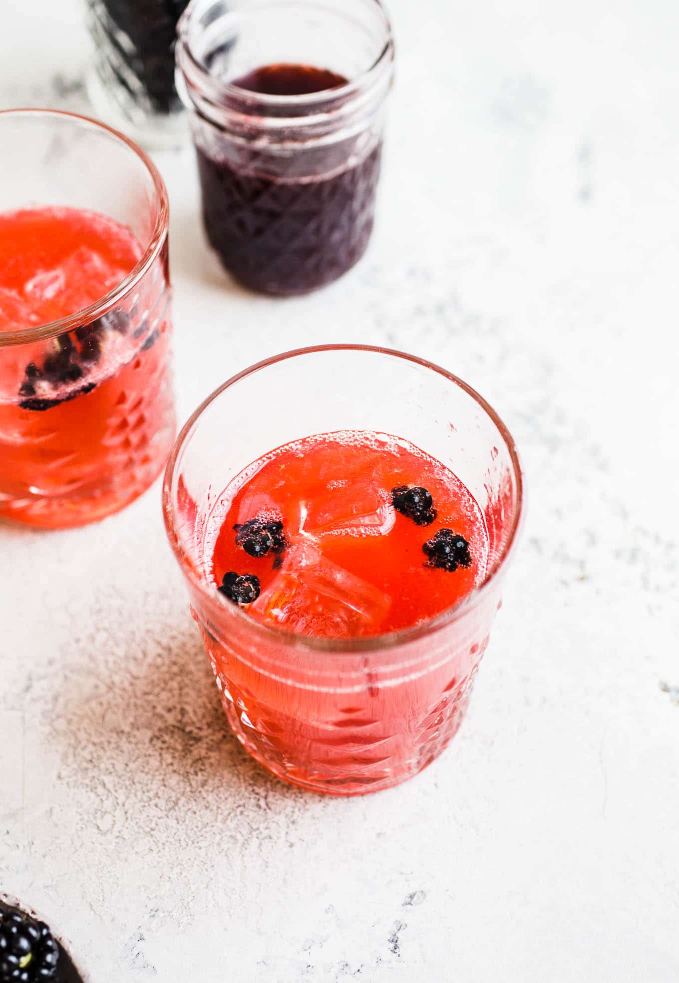 A dark pink cocktail in a glass with blackberries.