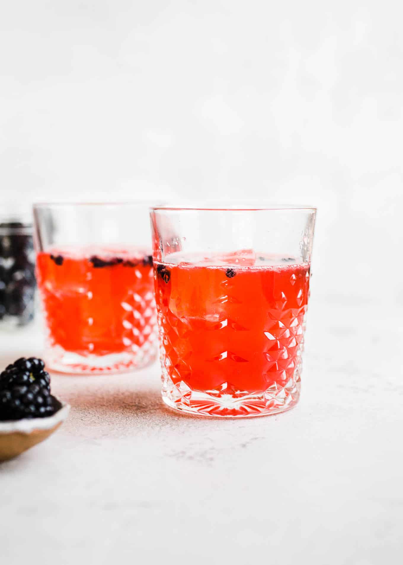 Two glasses with dark pink liquid and blackberries as garnish.