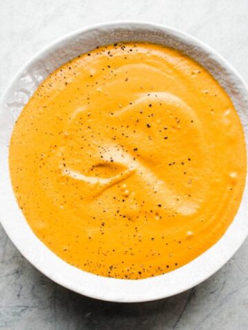 Red pepper cream sauce in a white bowl on a gray surface.